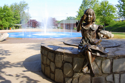 Statue of girl sitting in front of splash pad
