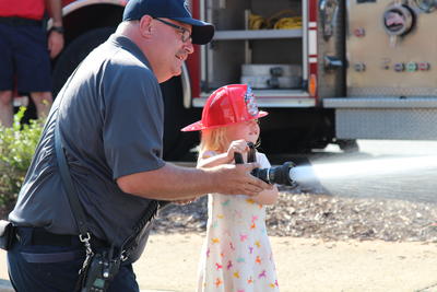 Firefighter training child on how to use a fire hose